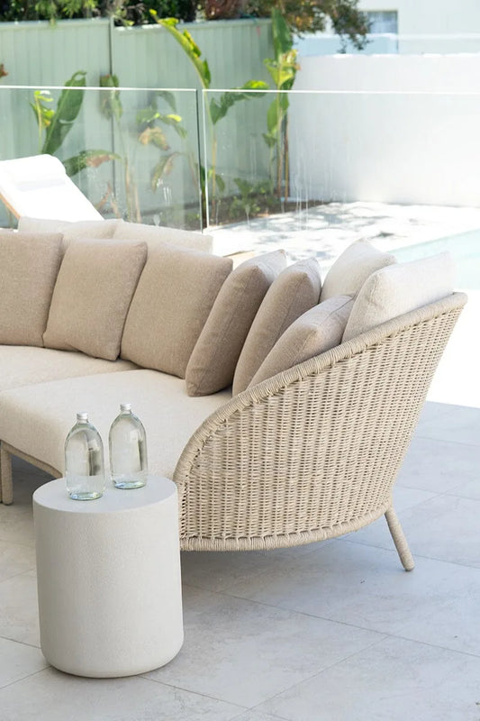 Beige outdoor sofa with wicker armrest and a small round table on a patio.