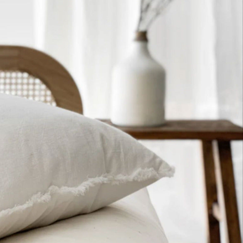 Chalk white ramie cushion cover with hand-finished fringe edges on modern neutral sofa