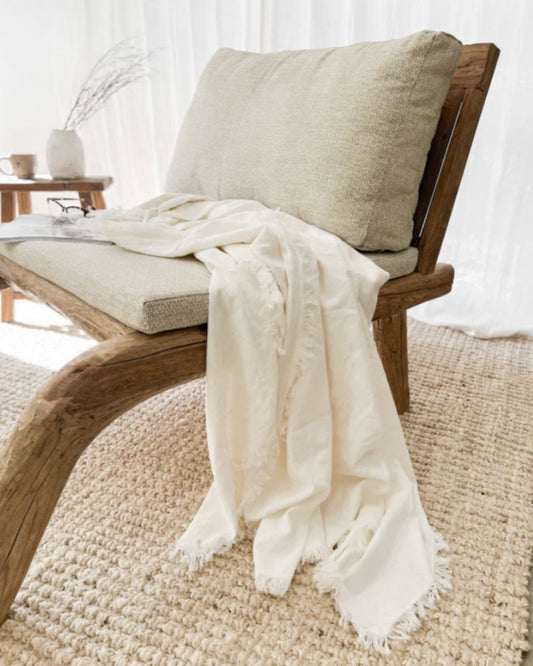 Wooden chair with a beige cushion and white blanket on a textured rug