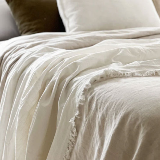 Neatly made bed with beige bedding and pillows in a softly lit room.
