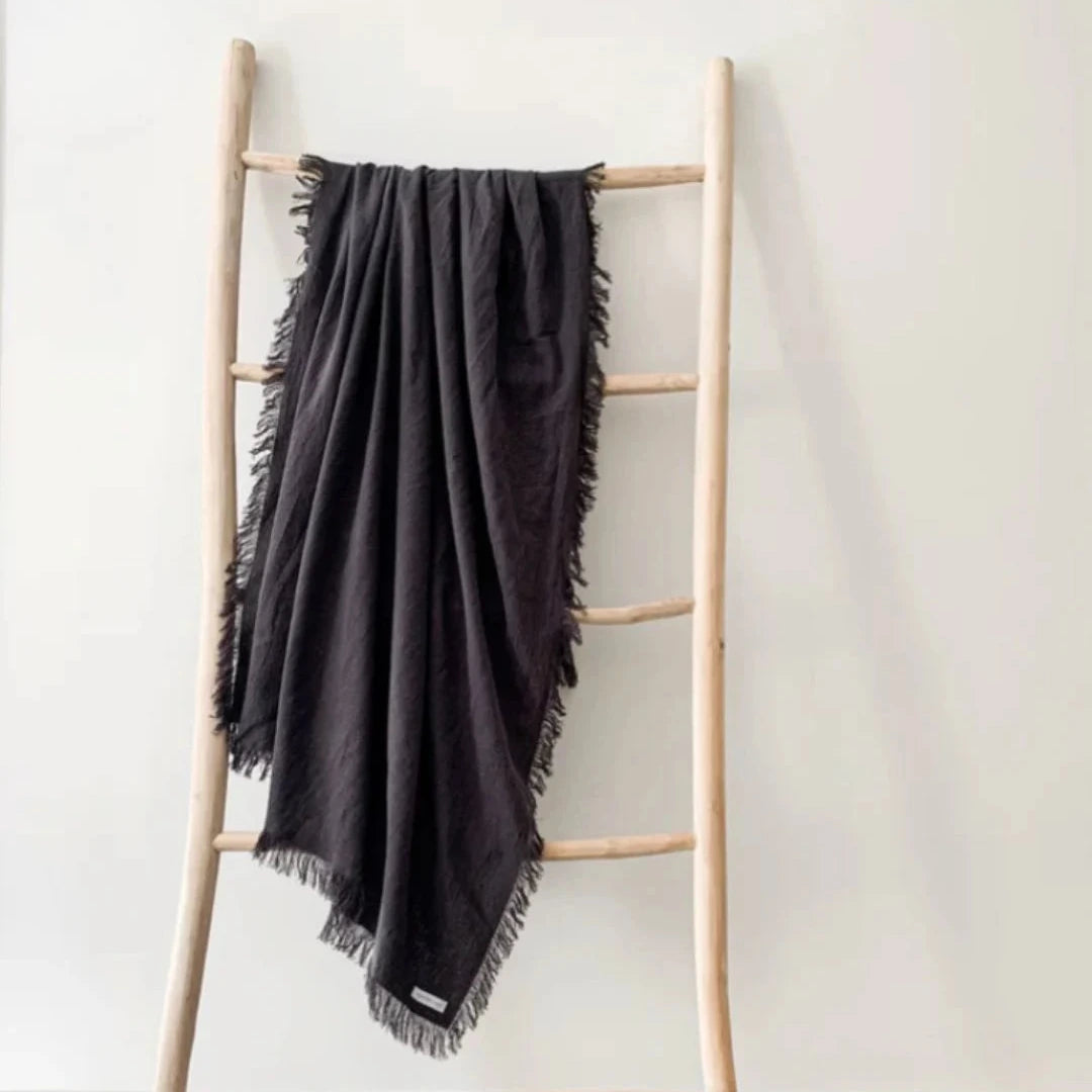 Black blanket draped over a wooden ladder against a white wall.