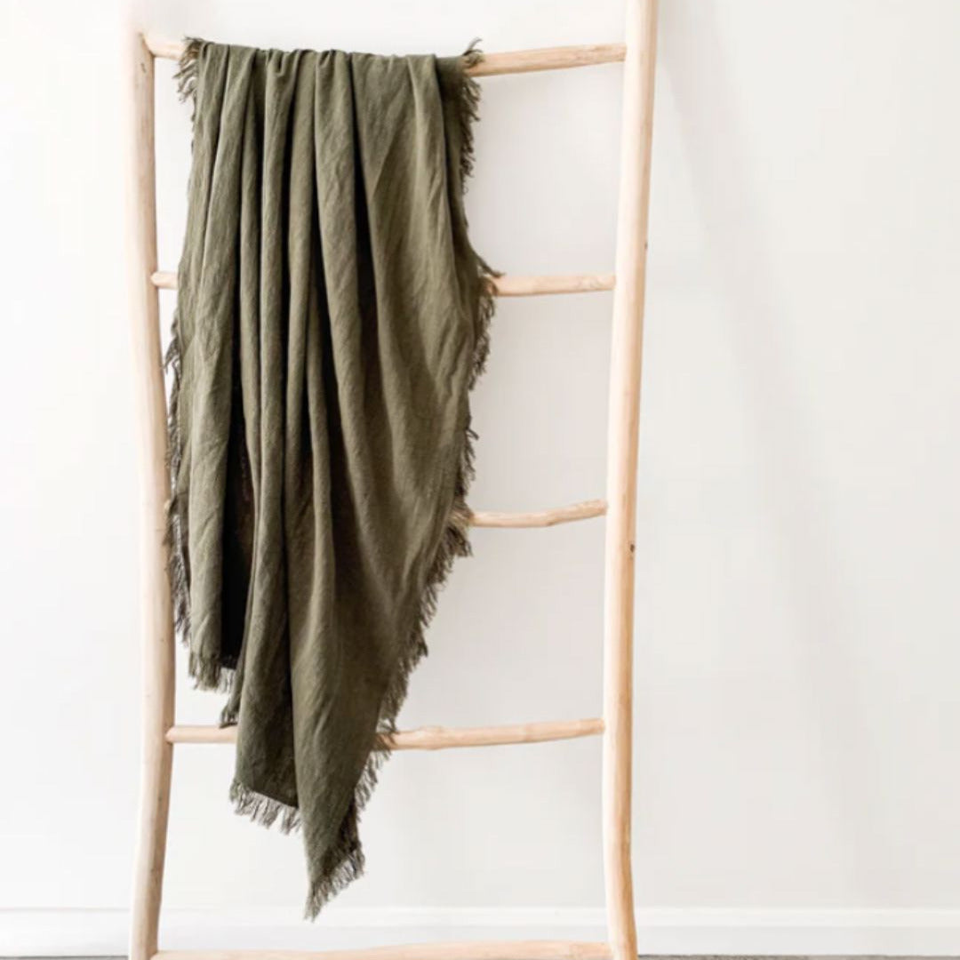 Green blanket draped over a wooden ladder against a white wall