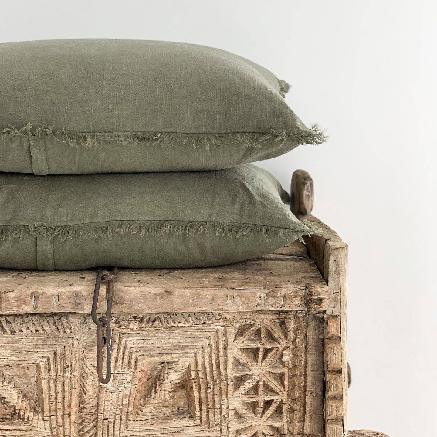 Two green pillows stacked on a wooden bench with intricate carvings against a white background