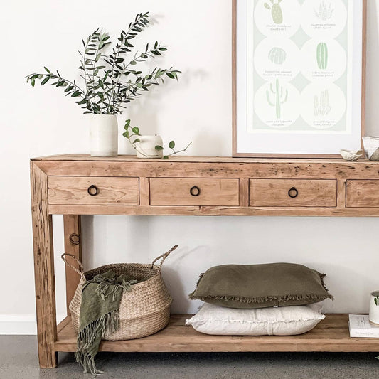 Wooden console table with decorative items including a plant, framed artwork, and pillows in a room.