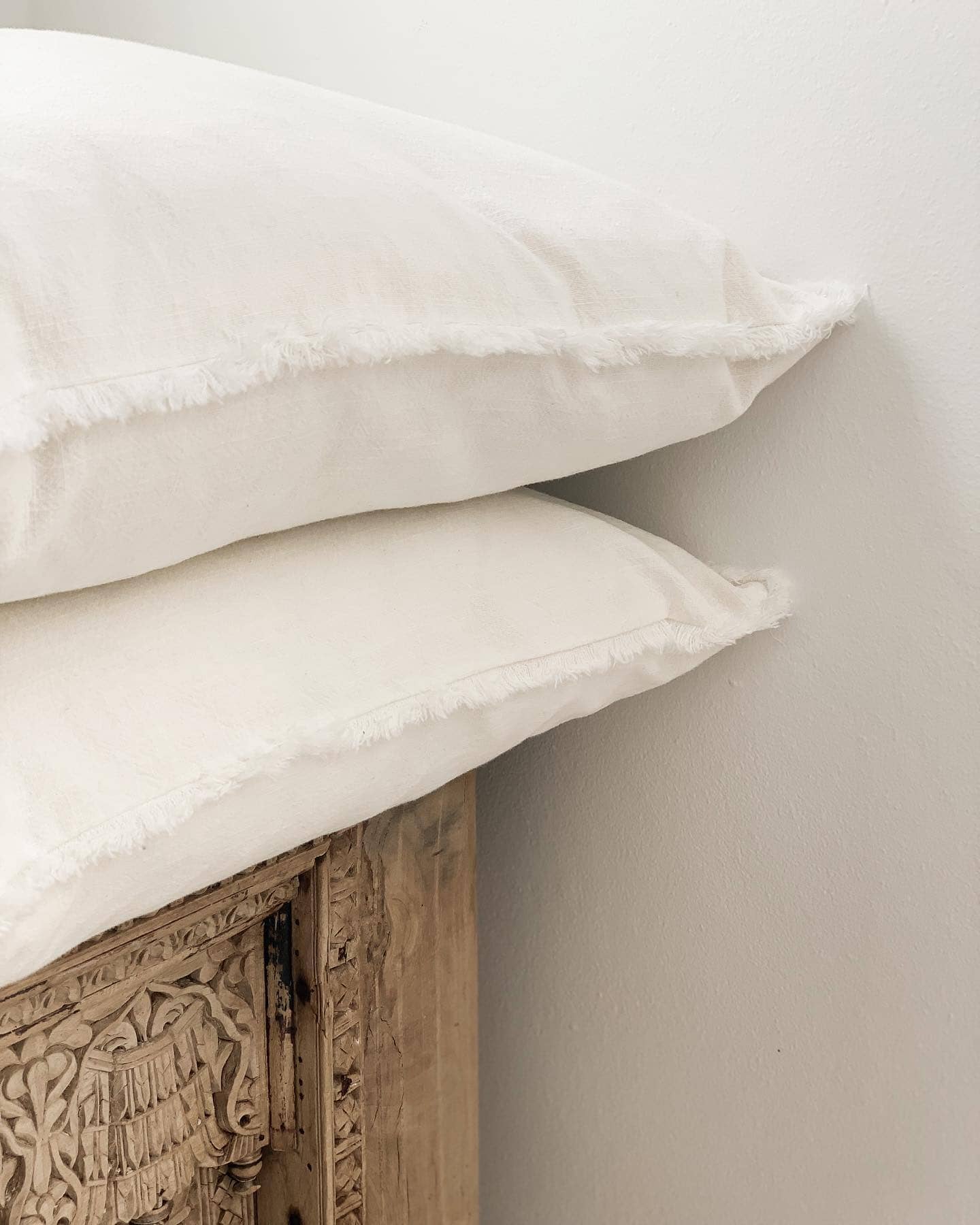 Two white pillows stacked on a wooden headboard against a light gray wall.