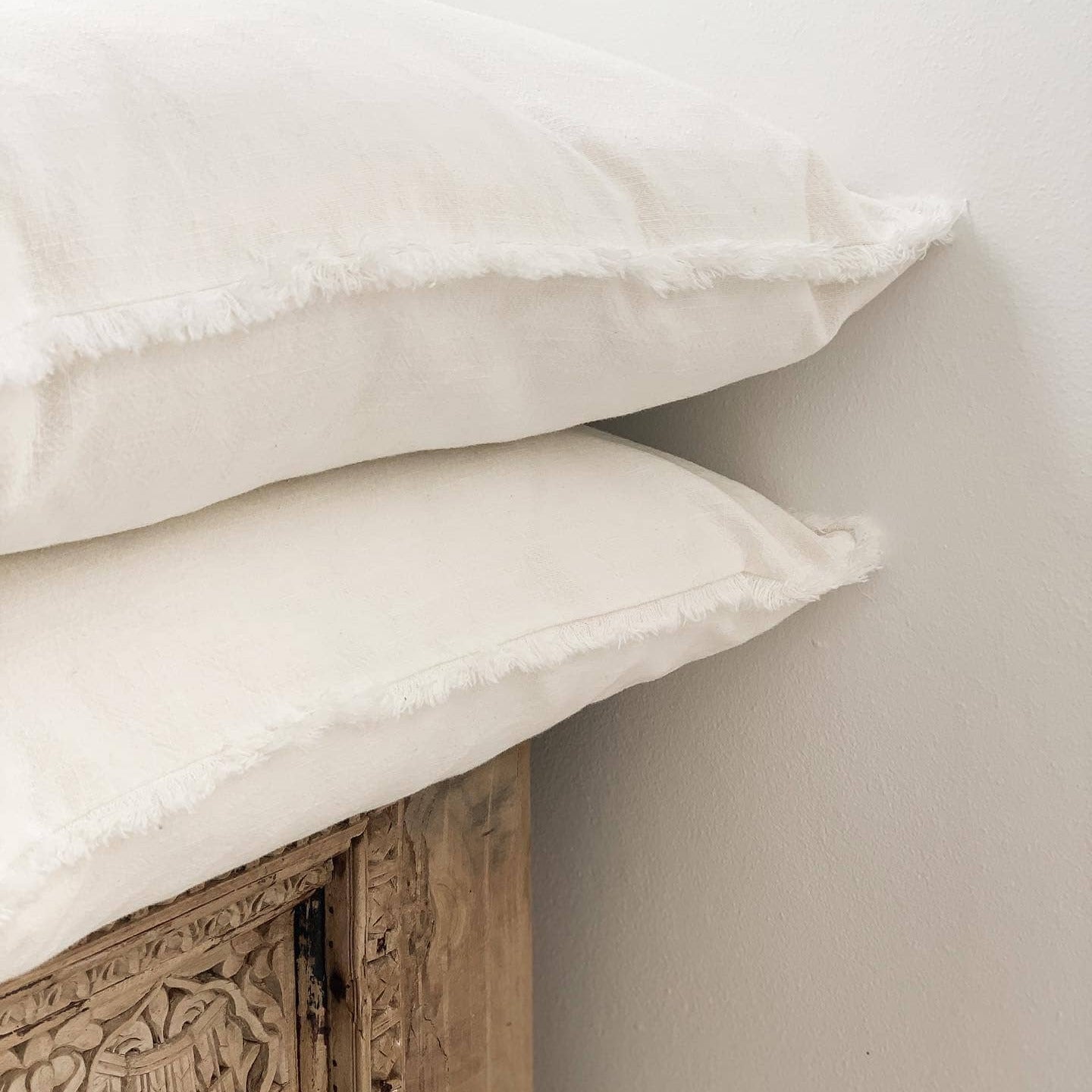 Two white pillows stacked on a wooden headboard against a light gray wall.