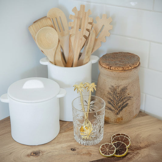 Wooden utensils in a container on a kitchen counter with a glass, lemon slices, and a decorative plant.