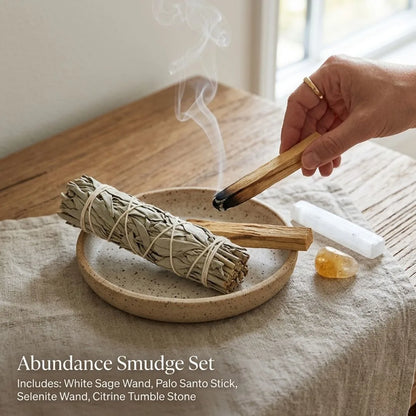 Person holding a wooden tool over a bundle of smudge sticks on a wooden surface.