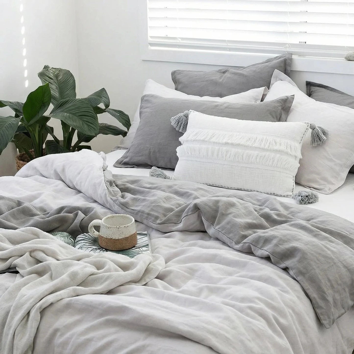 Neatly made bed with gray and white bedding in a bright room.