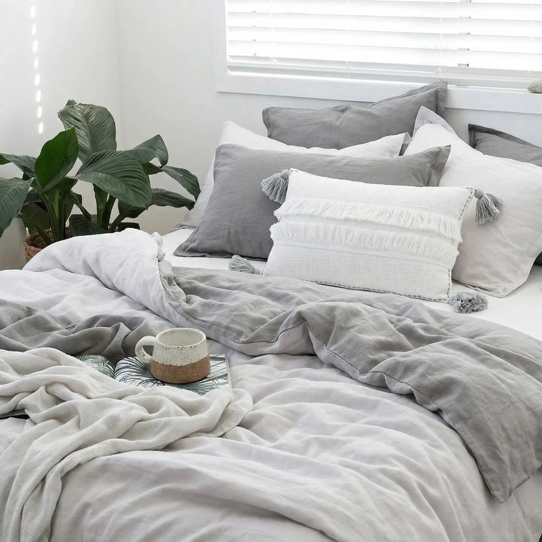 Neatly made bed with gray and white bedding in a bright room.
