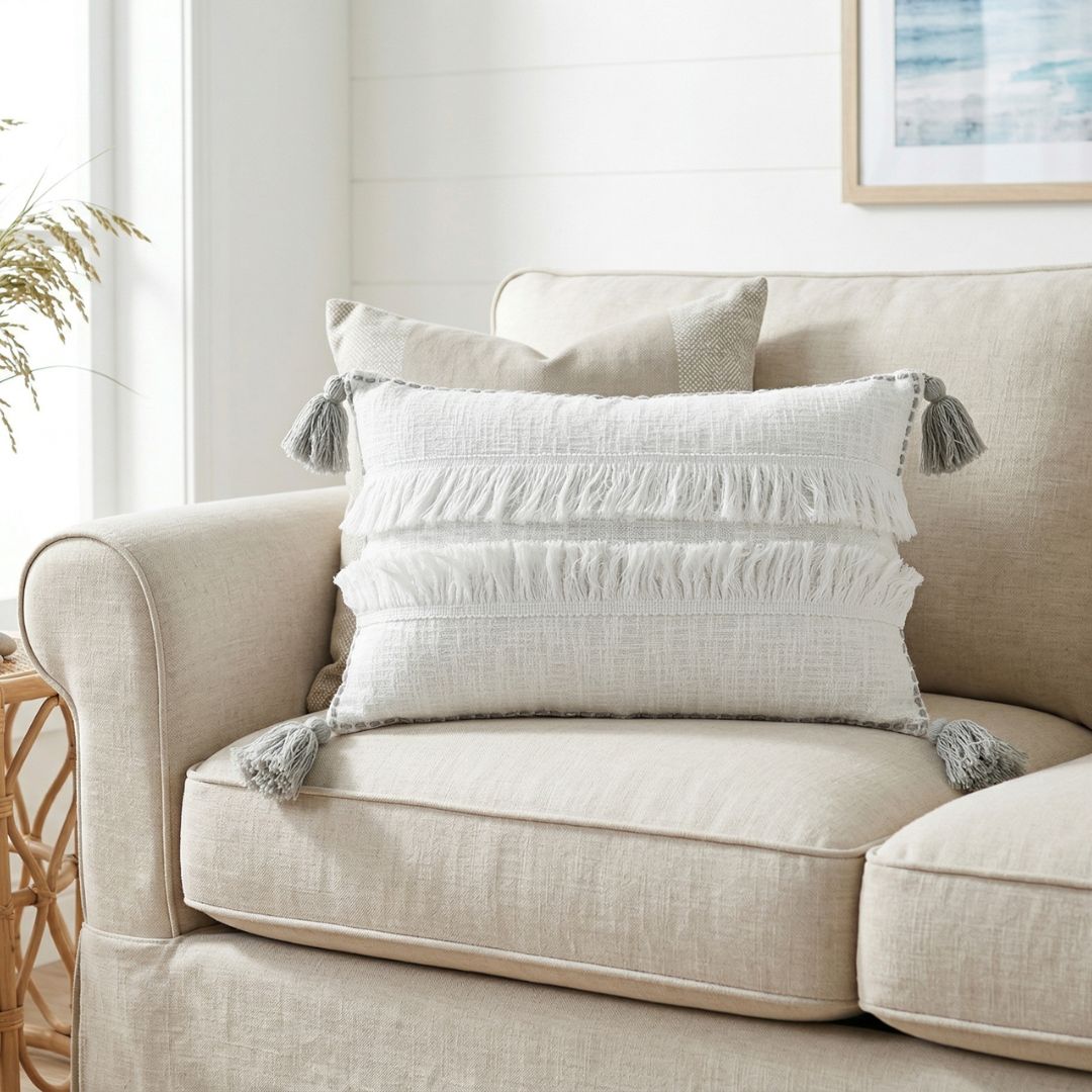 Beige sofa with decorative pillows featuring tassels in a living room setting.