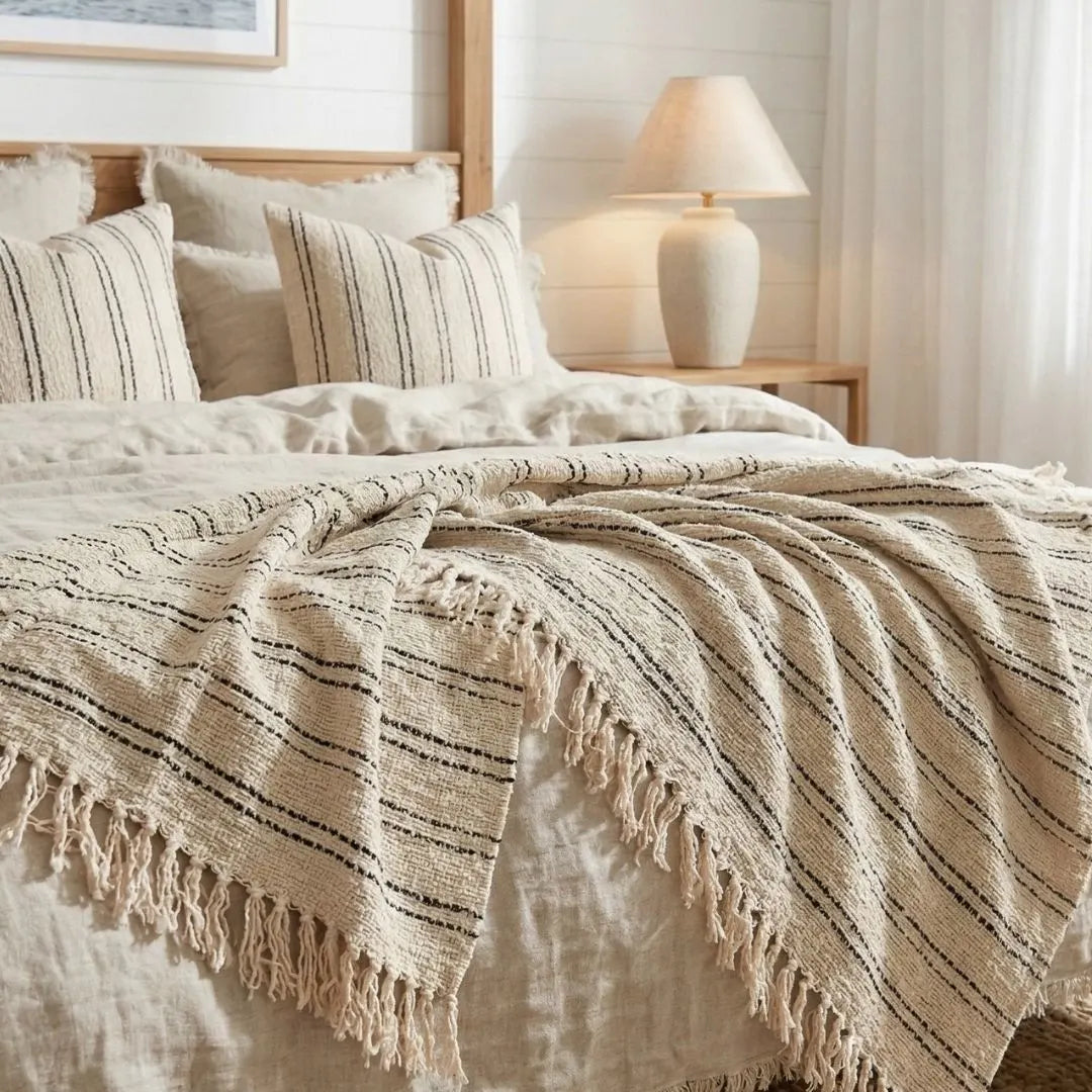 Beige striped blanket with tassels on a bed in a bedroom setting.