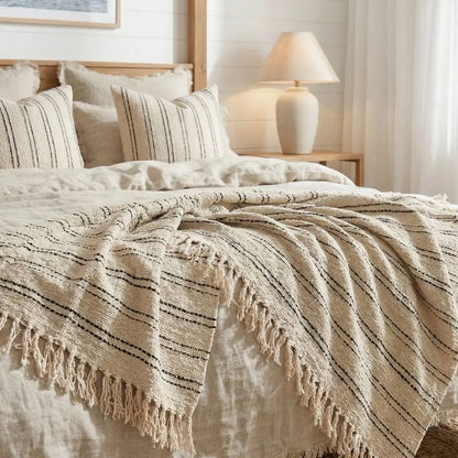 Beige striped blanket with tassels on a bed in a bedroom setting.