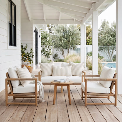 A 4-piece outdoor patio conversation set on a wooden deck under a white porch. The set includes a light wood frame, cream cushions, a matching 3-seater sofa, two armchairs, and a round wooden coffee table.