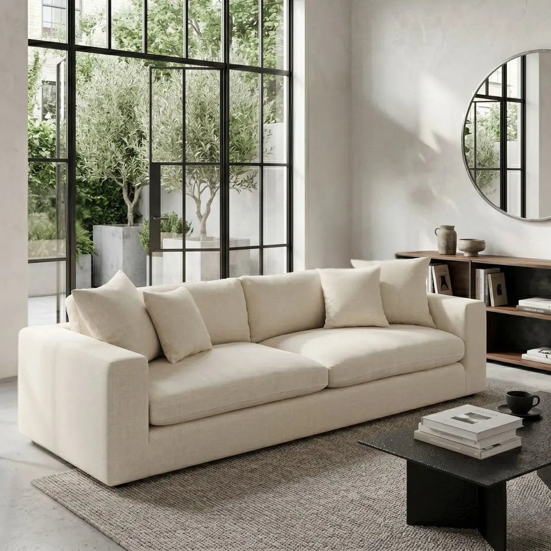 Beige sofa in a modern living room with large windows and a round mirror.