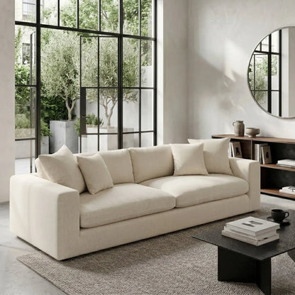 Beige sofa in a modern living room with large windows and a round mirror.