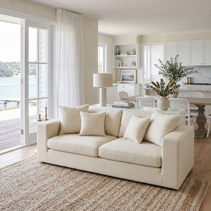 Beige sofa in a modern living room with large windows and a view of water.