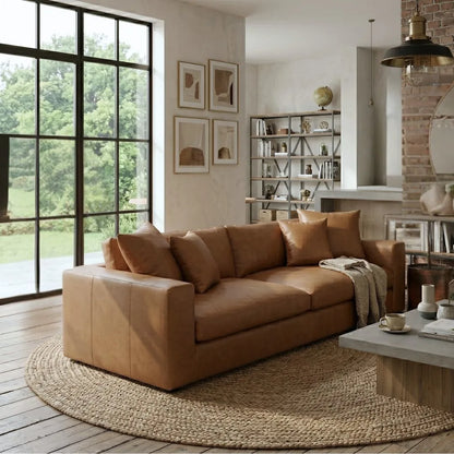 Brown leather sofa in a living room with large windows and a bookshelf.