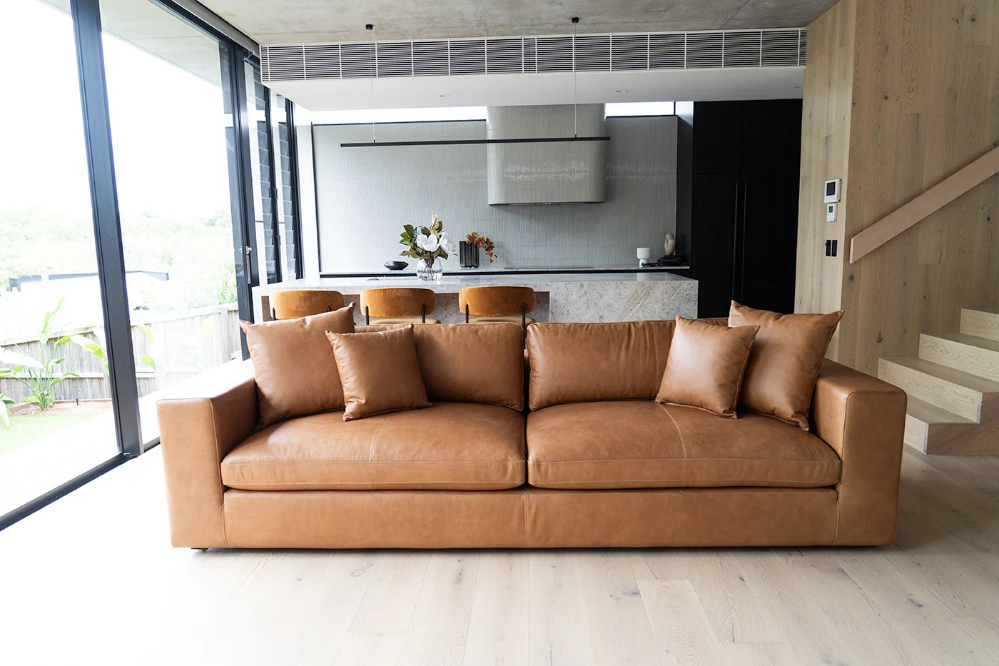 Brown leather sofa in a modern living room with a kitchen in the background.
