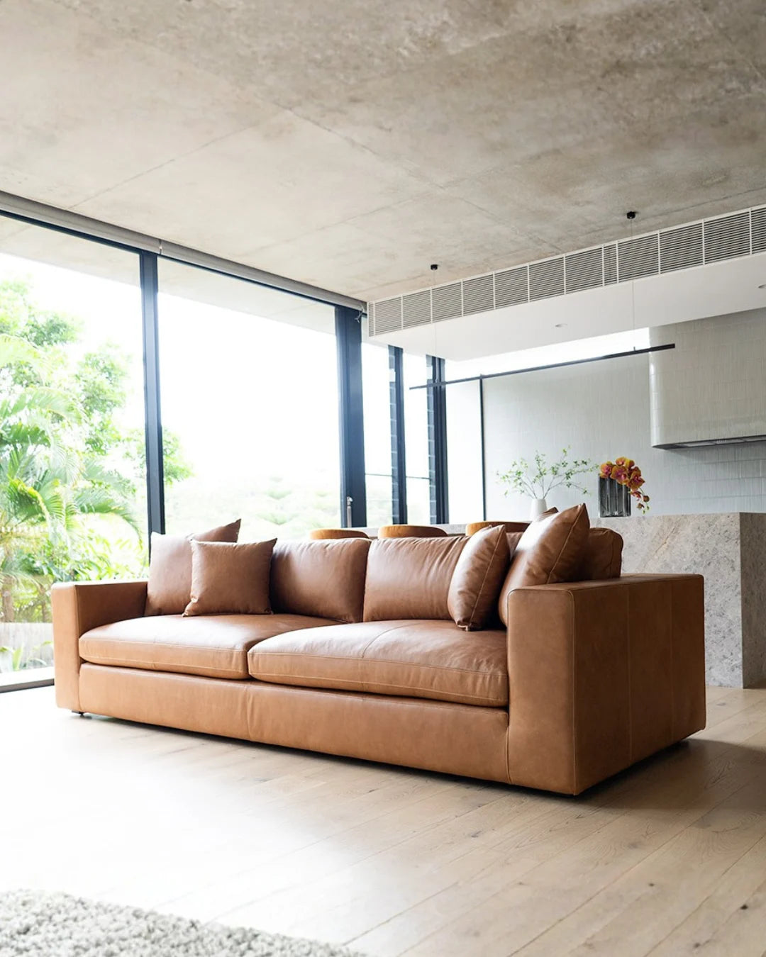 Brown leather sofa in a modern living room with large windows.