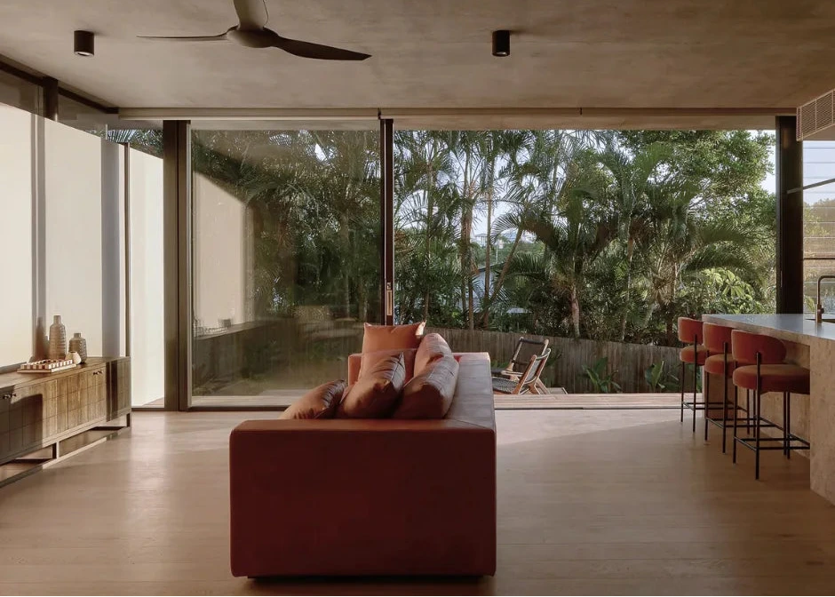 Modern living room with a brown leather sofa, large windows, and outdoor view.