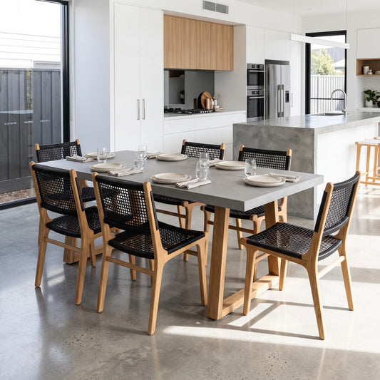 A modern dining table with a gray stone-look top and light wood frame, surrounded by six woven black and wood chairs, set in a bright contemporary kitchen and dining room.
