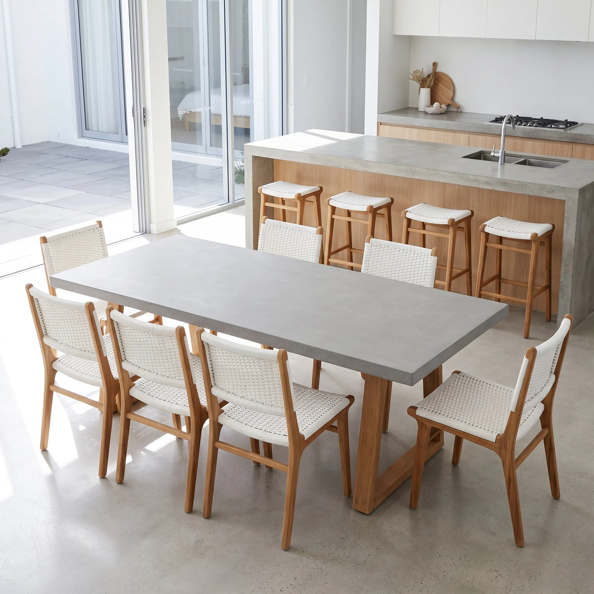A modern dining set featuring a rectangular concrete table and six wooden chairs with woven white seats, shown in a bright, contemporary kitchen and dining area.