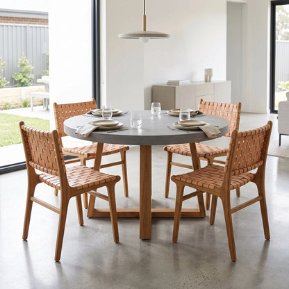 A round gray dining table with a wooden pedestal base, surrounded by four wooden chairs with woven tan seats and backs, set in a bright modern dining room.