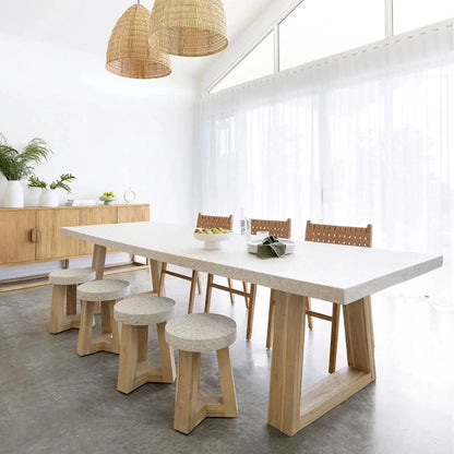 Modern dining area with a white table, wooden chairs, and stools in a bright room.