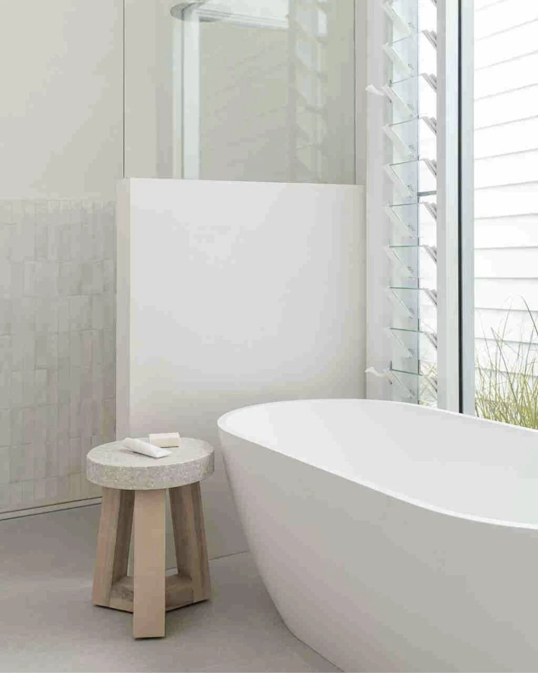 Modern bathroom with a freestanding bathtub and a small wooden stool.