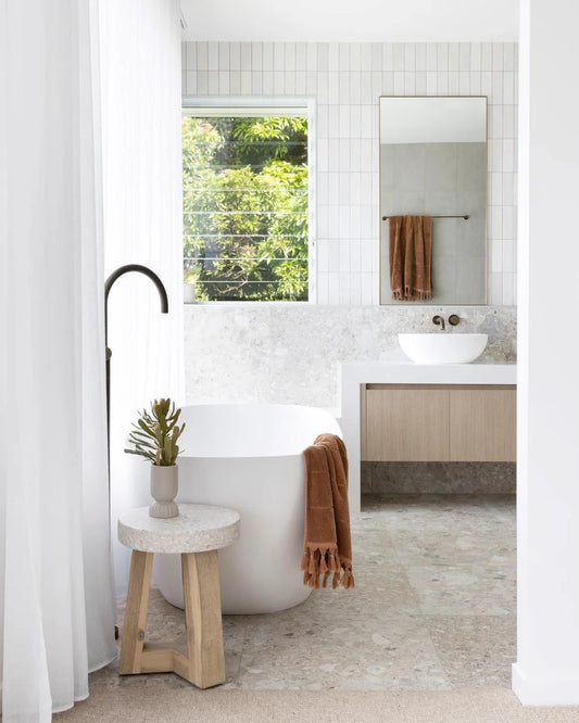 Modern bathroom with a freestanding bathtub, wooden stool, and mirror.