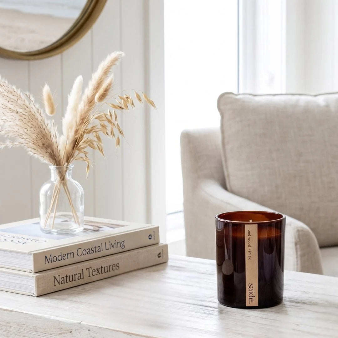 Candle and books on a table with a vase of pampas grass in a living room setting.