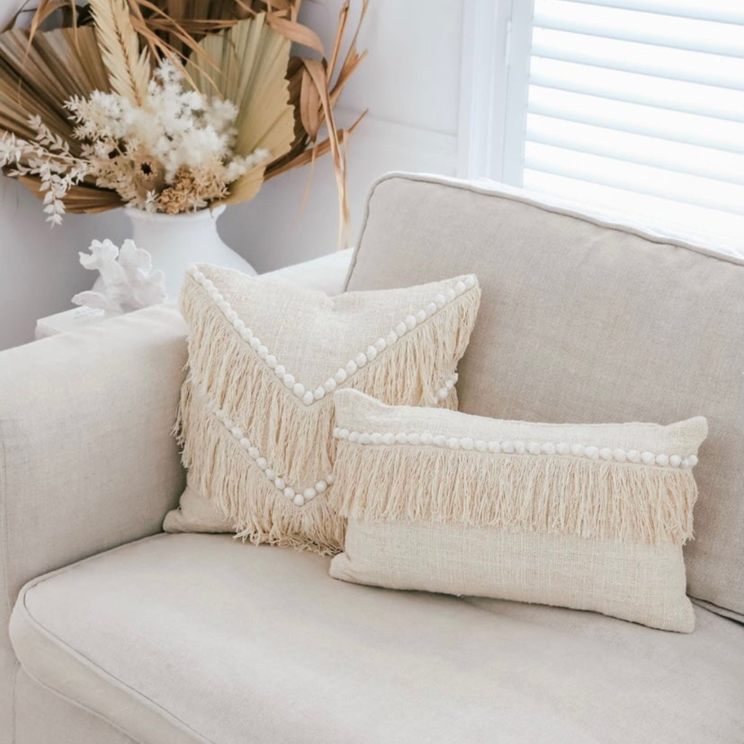 Beige sofa with decorative pillows and a vase of flowers in the background
