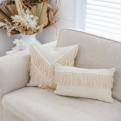 Beige sofa with decorative pillows and a vase of flowers in the background