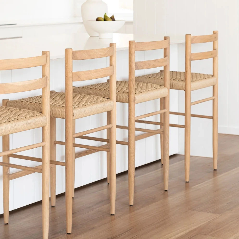 Four wooden bar stools with woven seats arranged around a white kitchen island.