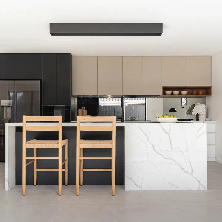 Modern kitchen with black cabinets, white island, and wooden chairs.