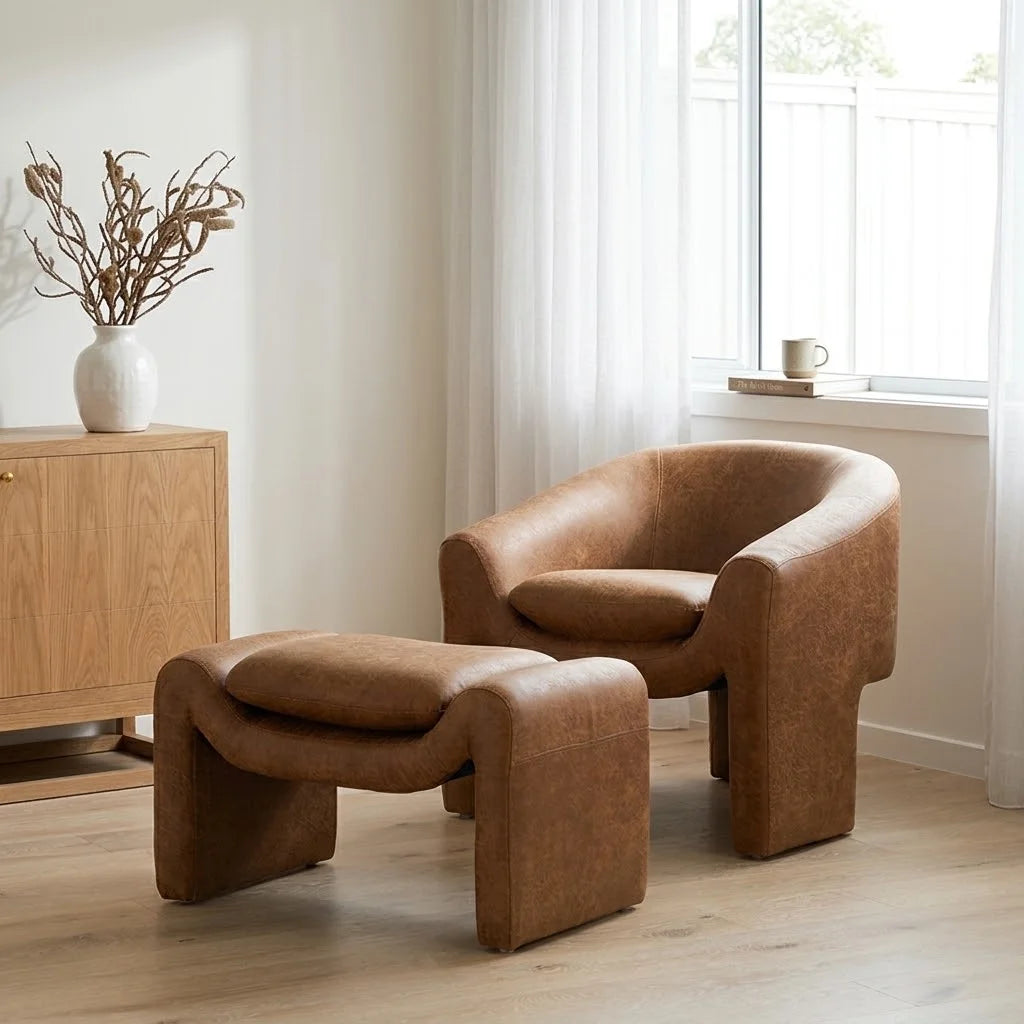 A brown leather armchair with a matching ottoman in a bright, modern room with a wooden sideboard and a window.
