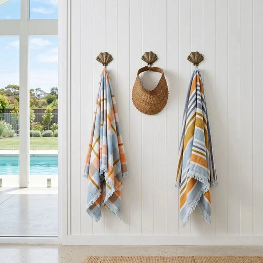 Two patterned towels hanging on hooks with a view of a pool outside.