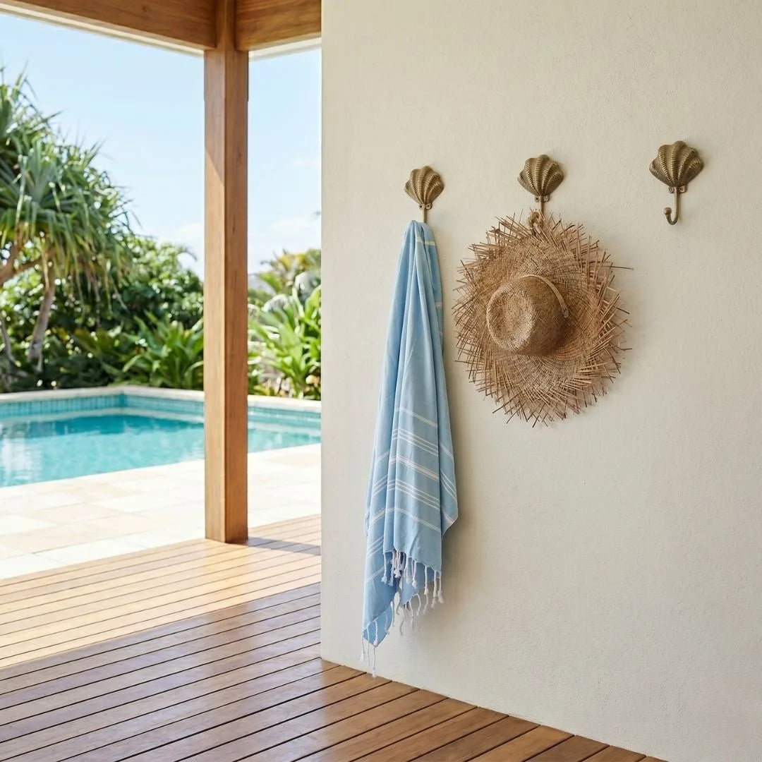 Blue towel and straw hat hanging on a wall with a pool view outside