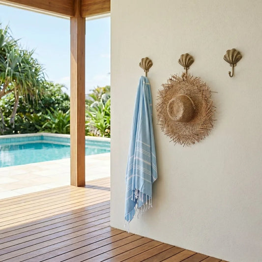 Blue towel and straw hat hanging on a wall with a pool view outside