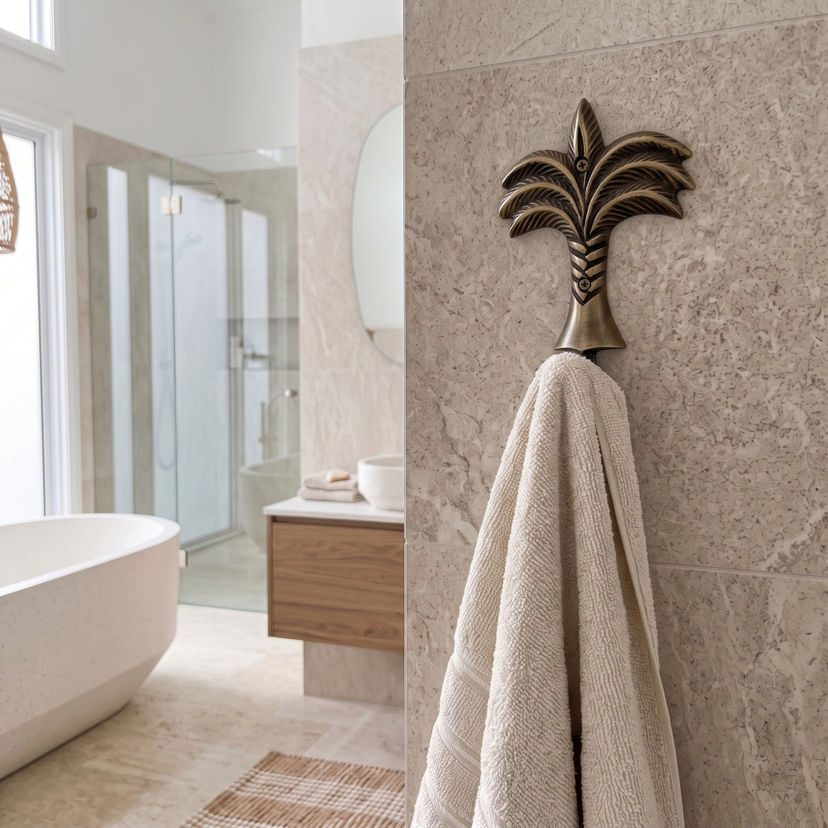 A textured beige towel hanging from a decorative bronze palm tree wall hook mounted on a beige marble bathroom wall.