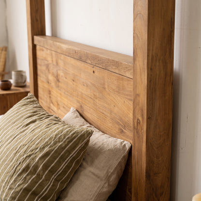 A close-up of a rustic wooden bed frame headboard and side rail with neutral-colored pillows in a bedroom setting.