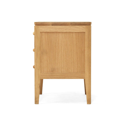 A light oak wood nightstand with three drawers on the left side, featuring a paneled front, tapered legs, and small round knobs, shown against a plain white background.