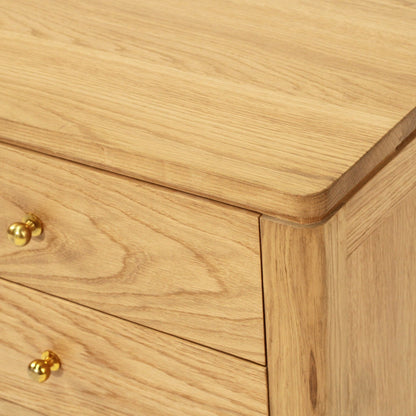Close-up of a light oak wood cabinet or dresser showing the grain, rounded corners, and two brass drawer knobs.