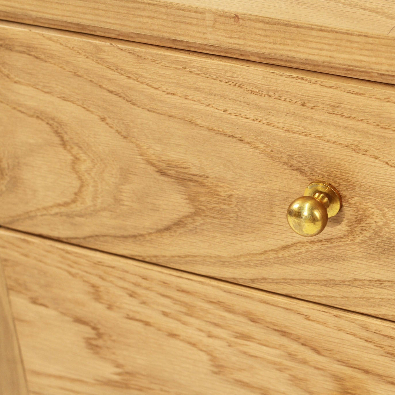 Close-up of a light oak wood drawer front with a round brass drawer knob.