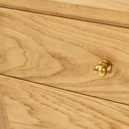 Close-up of a light oak wood drawer front with a round brass drawer knob.