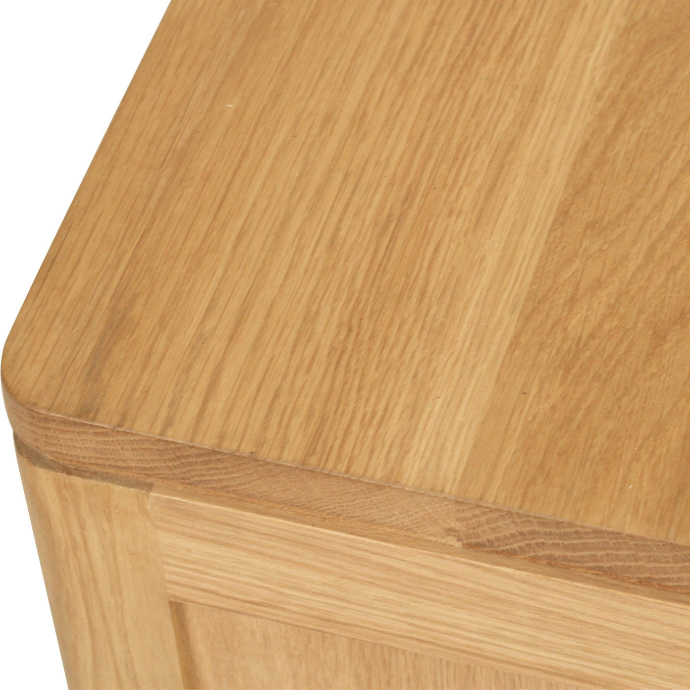 Close-up of a light oak wood cabinet corner showing the top surface, rounded edge, and front panel with visible wood grain.
