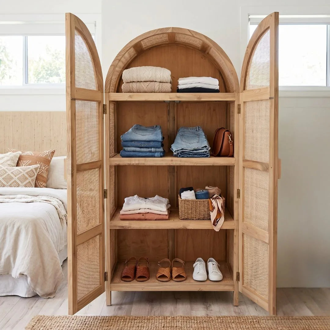 Wooden wardrobe with open doors displaying clothes and shoes in a bedroom setting.