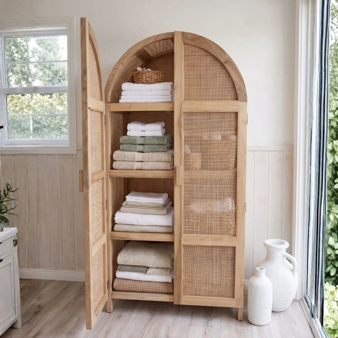 Wooden armoire with wicker doors containing folded towels in a bright room.