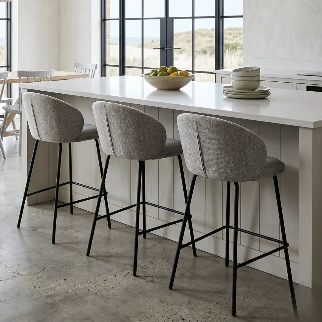 Modern kitchen with a white island, gray bar stools, and a view of the outdoors.